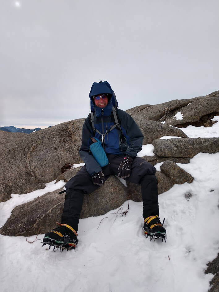 Man sitting on snowy rocks with crampons and hiking gear
